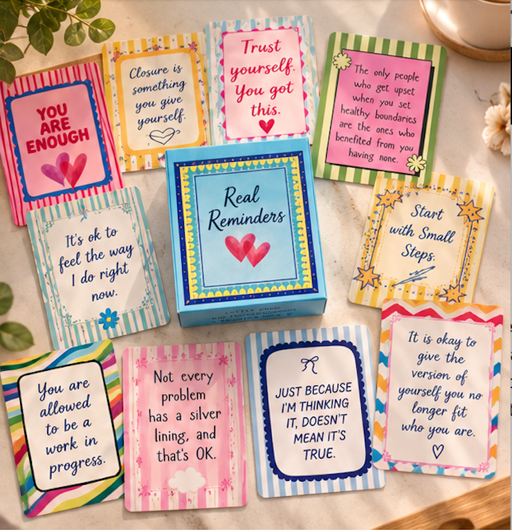 Thirty laminated Real Reminders affirmation cards laid flat, showing colourful wellbeing messages and designs.