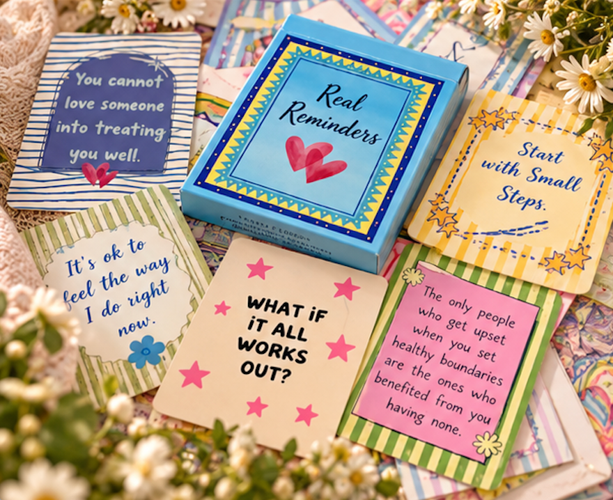 30 affirmation cards called "Real Reminders" surrounded by several colorful therapy-style cards with supportive messages, arranged on a soft floral fabric background.
